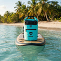 RIXVA 5L light blue waterproof dry bag with roll-top closure and exterior pocket sitting on a paddleboard at the beach